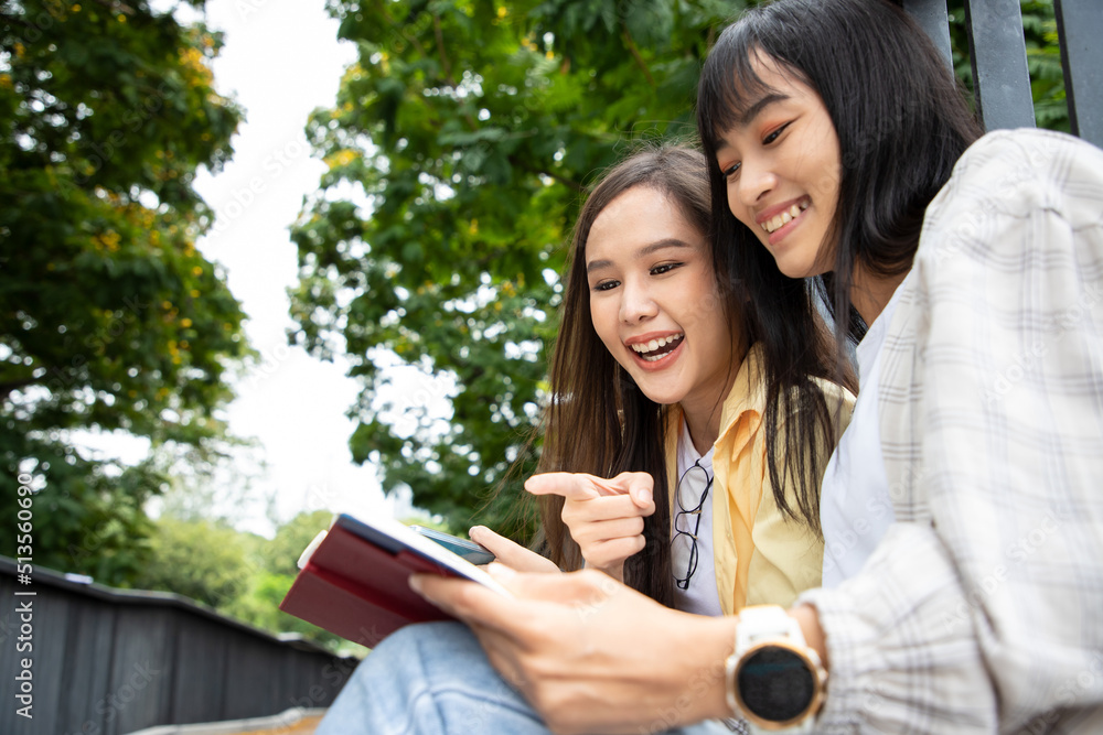 Learning outside classroom. Happy smiling young Asian woman with happy college friends in background at the summer park. Diversity of student doing homework and submit assignments to teachers. Learning outside classroom. Happy smiling young Asian woman with happy college friends in background at the summer park. Diversity of student doing homework and submit assignments to teachers.