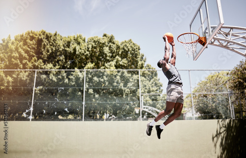 Full length of basketball player dunking a ball into the net during a match on a court. Fit and active athlete jumping to score during a competitive game. Healthy athletic african man in action