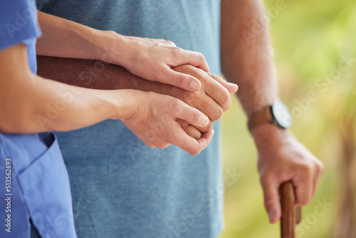 A nurse and senior patient holding hands while helping him to walk outside. Closeup of an elderly man being supported by female caregiver while walking to improve his mobility, health, and wellbeing