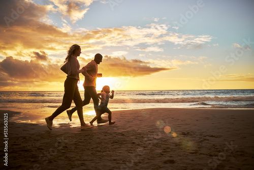 Silhouette of a carefree family running and having fun together during sunset on the beach. Parents spend time with their daughters on holiday. Little girl playing with her parents while on vacation #513563025