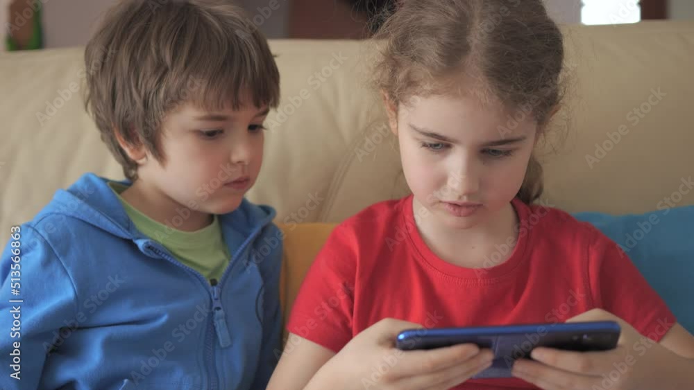 Children Playing Games In Phone at Home on Couch. Kids Playing Video Game on Mobile Phone. Boy and Girl Plays Video Game Smartphone on Sofa Friends Using Phone for Gaming Online Education Social Media Children Playing Games In Phone at Home on Couch. Kids Playing Video Game on Mobile Phone. Boy and Girl Plays Video Game Smartphone on Sofa Friends Using Phone for Gaming Online Education Social Media