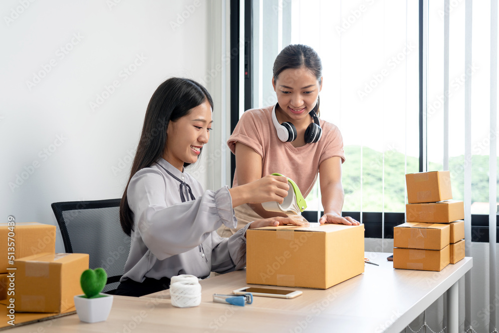 Two woman small business entrepreneur working at home receive ordering from online customer and checking data while preparing to packing product deliver sending to client Two woman small business entrepreneur working at home receive ordering from online customer and checking data while preparing to packing product deliver sending to client