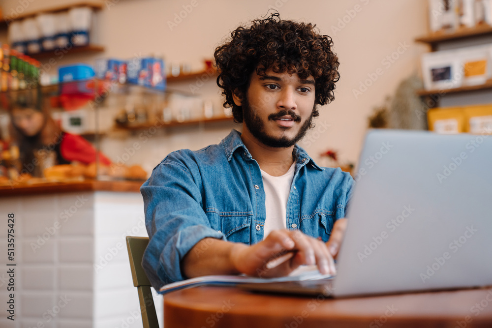 Young calm handsome indian man working with laptop at cafe Young calm handsome indian man working with laptop at cafe