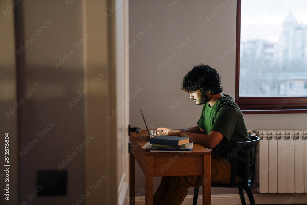 Young indian curly man sitting by table with laptop