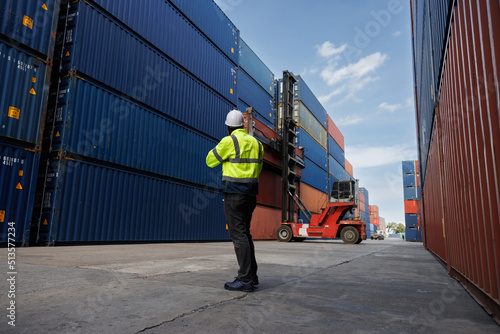 the african woker using walky talky comunicate with lifting container team with blue sky. Logistics transportation industry forklift handling container box loading stacker. back side view. photo