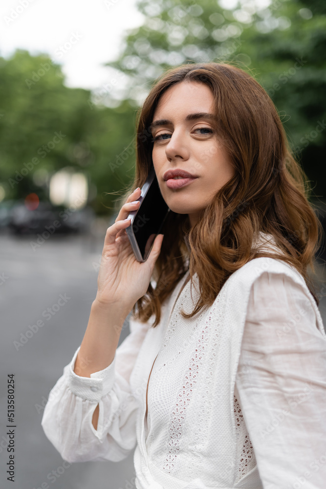 Brunette woman talking on smartphone and looking at camera on street in Paris. Brunette woman talking on smartphone and looking at camera on street in Paris.
