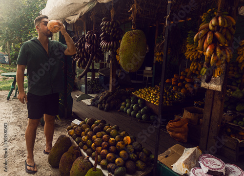 Male model, traveler drinking coconut against the backdrop of an exotic fruit shop, holiday landscape. photo