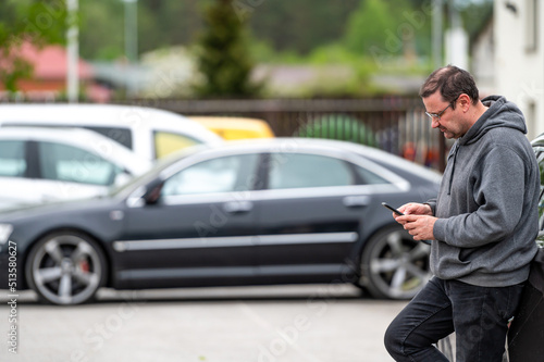man with smartphone standing next to the car, using mobile app for paying, car lock or Internet
