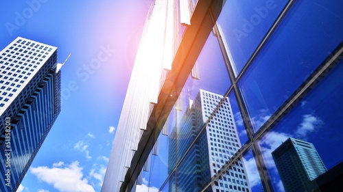 Blue sky reflection in glass facade of building. View of office building windows close up with sunrise  reflection and perspective..Bright sunny day with sunbeams on the blue sky.Velvia graphic filter