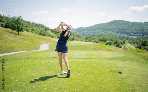 Pretty sportswoman hitting the ball with golf club. Professional female golfer holding golf club on field and looking away. Young woman standing on golf course on a sunny day.