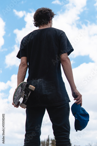A boy from the back posing while holding his skateboard and his cap