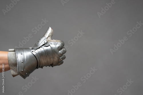 Photo Male hand in plate armor mitten shows a thumbs up gesture on the gray background close up