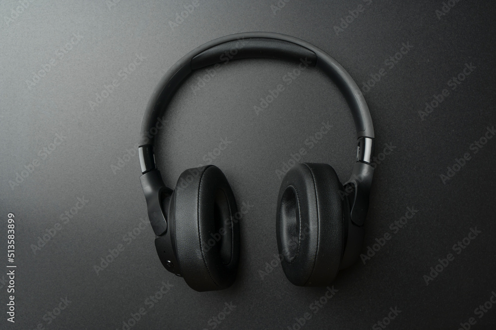 Headphones on a black background. Stylish studio headphones for listening to music, sounds, radio and podcasts lie on an empty dark table. Headphones on a black background. Stylish studio headphones for listening to music, sounds, radio and podcasts lie on an empty dark table.