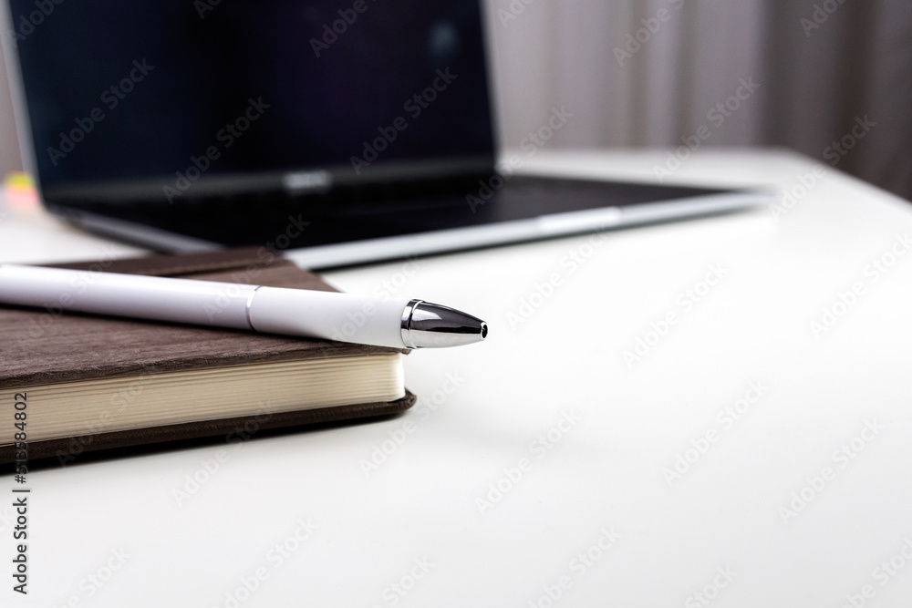 White office desk with notebook, pen and laptop. Selective focus. White office desk with notebook, pen and laptop. Selective focus.