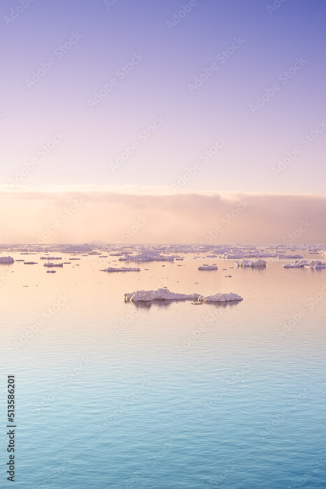 Seascape with floating glaciers at dawn. Serene winter arctic landscape. Icebergs on calm sea horizon at sunset in Denmark. Colorful nature scene of midnight sun. Polar summer in Ilulissat Greenland