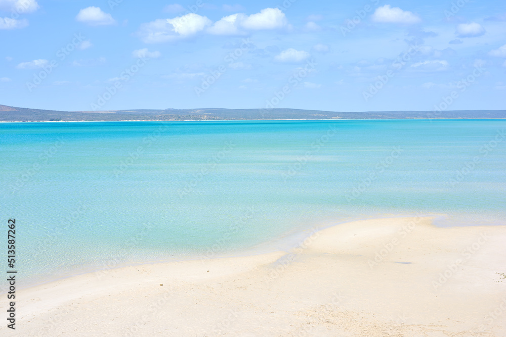 A clear beach during summer with a cloudy sky. Blue ocean water at the seashore on a hot day. Beautiful tropical scenery or seascape with mountains in the background. Landscape vacation destination