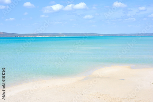 A clear beach during summer with a cloudy sky. Blue ocean water at the seashore on a hot day. Beautiful tropical scenery or seascape with mountains in the background. Landscape vacation destination