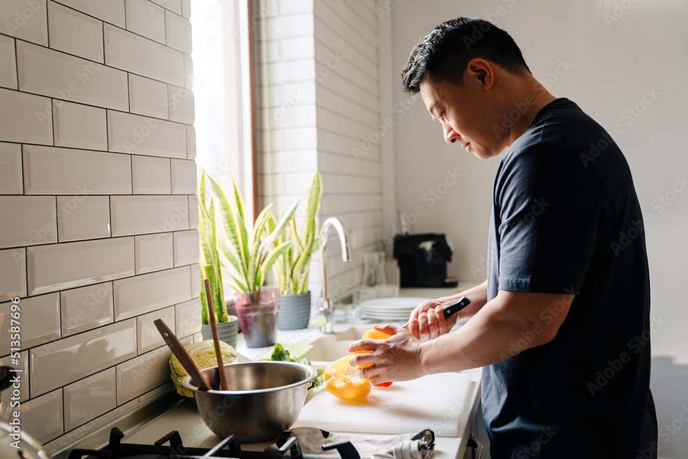 Adult asian man cutting vegetables and cooking in cozy kitchen Adult asian man cutting vegetables and cooking in cozy kitchen