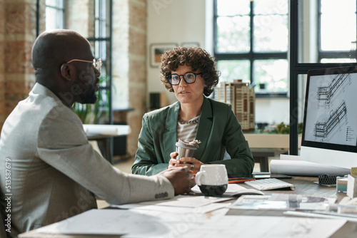 Female architect discussing construction project with her client while they sitting at table with computer