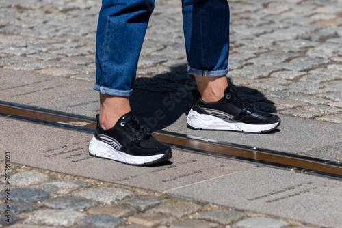Pair of feet with black sneakers standing on both sides of meridian line on ground at Greenwich observatory.