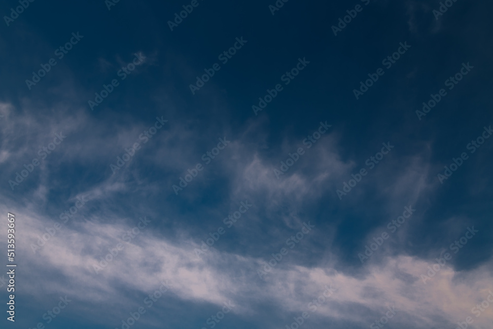 Picturesque cloudscape background with light spindrift clouds on a dark blue sky