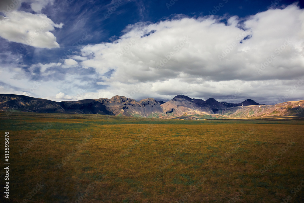 Fototapeta premium Vast moss-covered lava field with mountains in the distance in a cloudy blue sky background