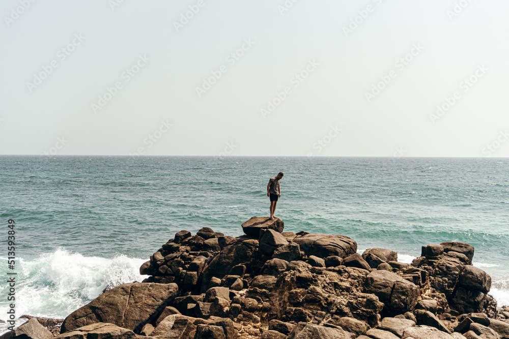 Male model, traveler standing on the rocks against the sky and ocean, holiday landscape.