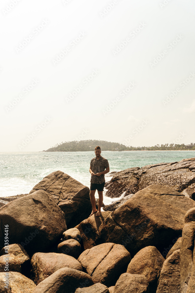 Male model, traveler standing on the rocks against the sky and ocean, holiday landscape.