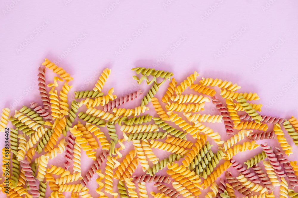 Beautiful Italian uncooked colored farfalle pasta close-up on pink background. horizontal top view