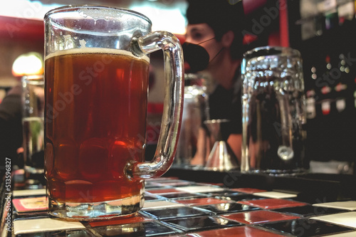 Closeup of big beer mug glass and young latin bartender in the bar from a pub in the night