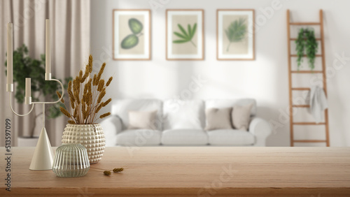 Wooden table, desk or shelf close up with ceramic and glass vases with dry plants, straws over blurred view of scandinavian living room with sofa, modern interior design concept