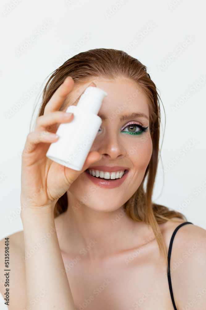 Close up of smiling Beautiful redhead woman with empty mockup cream bottle on white background with copy space. Close up of smiling Beautiful redhead woman with empty mockup cream bottle on white background with copy space.