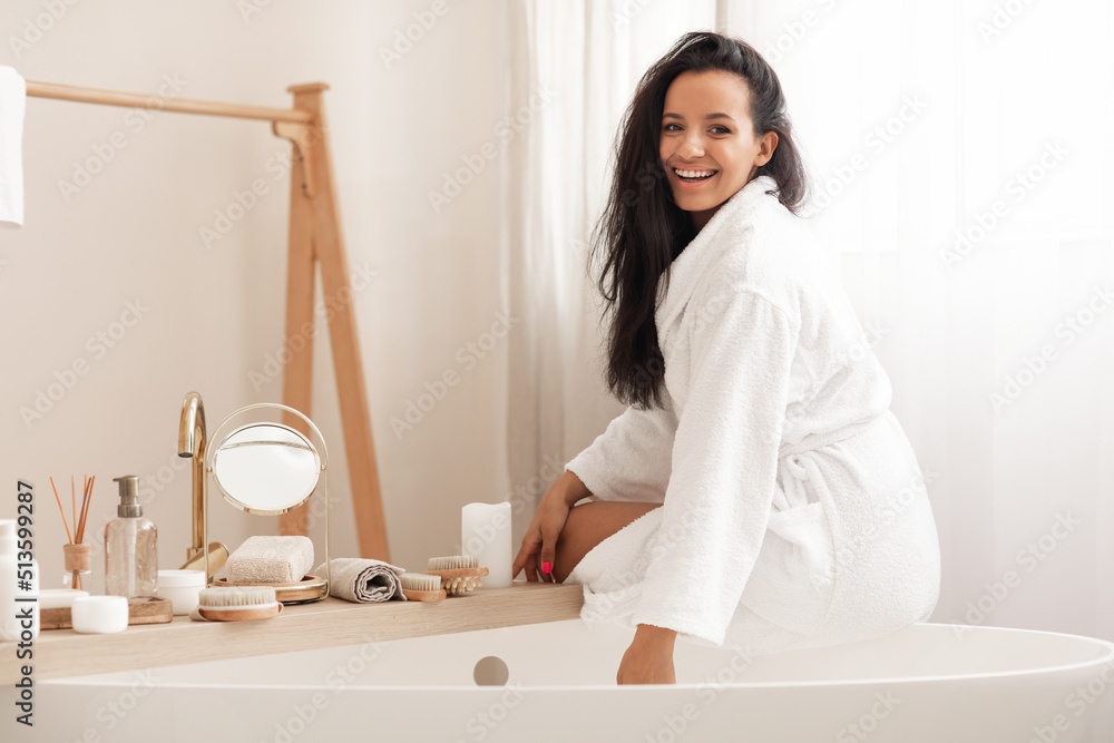 Cheerful Attractive Lady Wearing Bathrobe Sitting On Bathtub In Bathroom Cheerful Attractive Lady Wearing Bathrobe Sitting On Bathtub In Bathroom