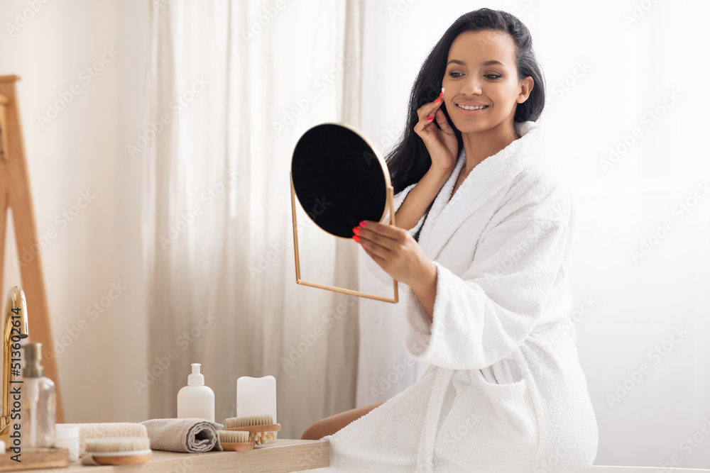 Cheerful Black Female Applying Moisturizer Looking At Mirror In Bathroom Cheerful Black Female Applying Moisturizer Looking At Mirror In Bathroom
