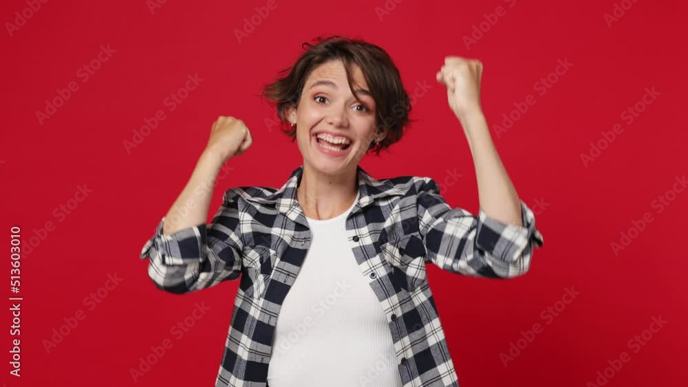 Excited jubilant happy young woman 20s she wearing casual clothes doing winner gesture celebrate clenching fist say yes isolated against over plain solid dark red color wall background studio portrait Excited jubilant happy young woman 20s she wearing casual clothes doing winner gesture celebrate clenching fist say yes isolated against over plain solid dark red color wall background studio portrait