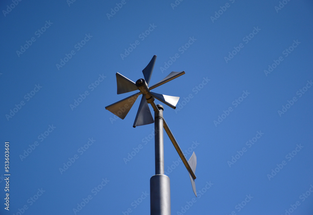Anemometer wind speed indicator and measuring device. stainless steel tube post. wind vane, weather vane or wind cock. meteorological device. abstract low angle view. triangular blades. clear blue sky Anemometer wind speed indicator and measuring device. stainless steel tube post. wind vane, weather vane or wind cock. meteorological device. abstract low angle view. triangular blades. clear blue sky