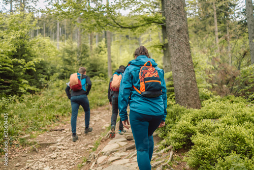 Young man and woman with backpack and sportswear hiking in mountains during summer season, traveler walking in the forest. Travel, adventure and journey concept. 