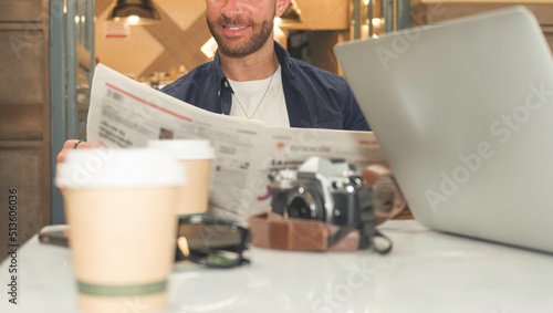 Unrecognizable Caucasian man placidly reading a newspaper sitting at a table in a coffee shop. photo