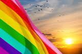 Waving LGBT pride flag on sunset sky with flying birds, rainbow flag background. Multicolored peace flag movement. Original colors symbol. 3d-rendering.