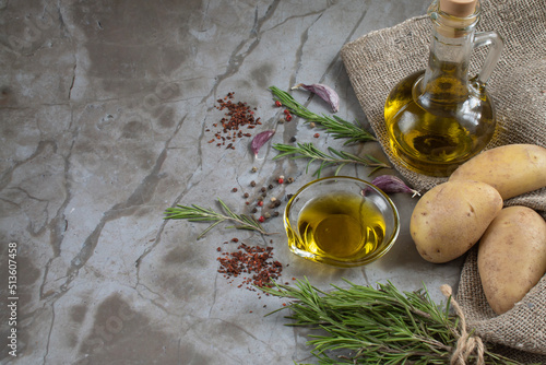 Ingredients for delicious baked potatoes in a rustic way: potatoes, garlic, olive oil, rosemary, dried tomatoes, multicolored pepper. Natural background. Copy space