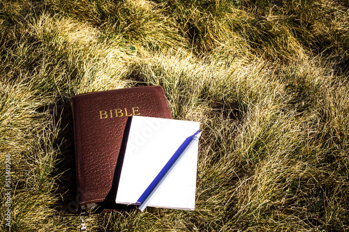 Outdoor Bible study during mountain hike in the fall. Bible, empty notepad and a pencil on a dry grass ground background.
