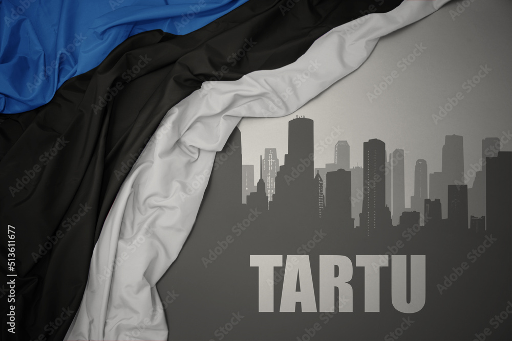 abstract silhouette of the city with text Tartu near waving national flag of estonia on a gray background.