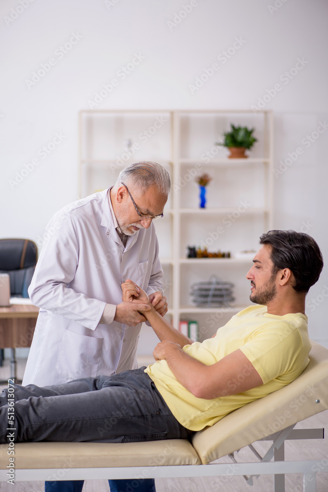 Young male patient visiting old male doctor chiropractor Young male patient visiting old male doctor chiropractor