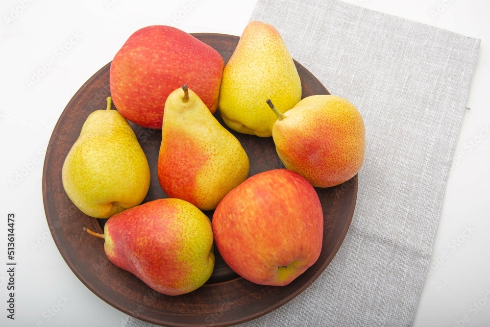 Close-up of ripe pears and apples in a clay plate on a white background. Top view. Close-up of ripe pears and apples in a clay plate on a white background. Top view.
