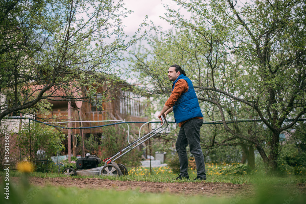 Portrait of a young farmer, gardener with a lawn mower on a plot of land in spring. Portrait of a young farmer, gardener with a lawn mower on a plot of land in spring.