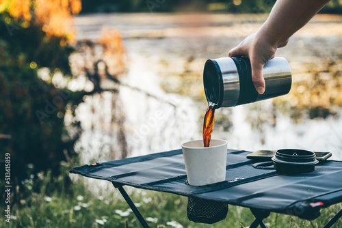 Print op canvas Pouring hot black coffee in reusable bamboo cup on camping table outdoors during early morning hours