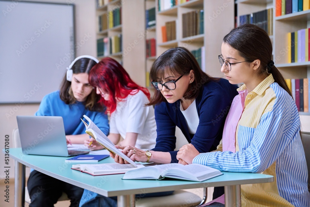 Group of teenage students and teacher study at desk in library Group of teenage students and teacher study at desk in library