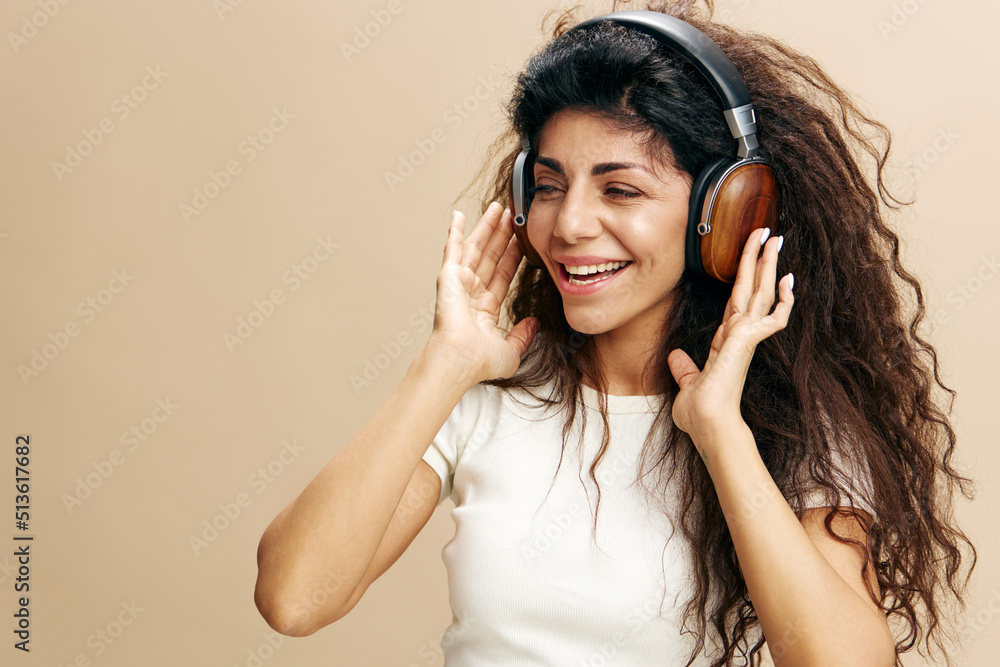 TALENT CONCEPT. Overjoyed Latin lady with headphones posing isolated, listening to music and singing, enjoying cool playlist and moving to favorite song over beige background. Copy space. Mockup TALENT CONCEPT. Overjoyed Latin lady with headphones posing isolated, listening to music and singing, enjoying cool playlist and moving to favorite song over beige background. Copy space. Mockup