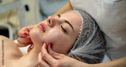 Beautiful young woman having curative facial cheeks massage in beauty salon.