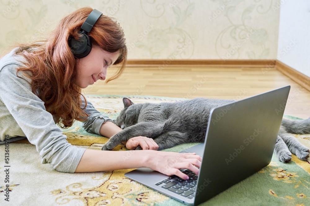 Preteen girl in headphones with laptop and sleeping gray cat